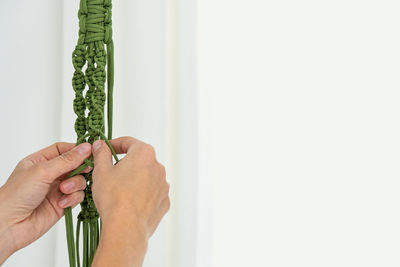 Handmade green macrame plant hangers with potted plant are hanging on woman hand. pot and monstera