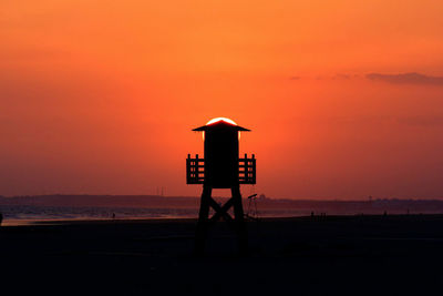 Lifeguard hut on beach against orange sky