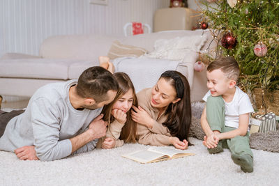 Happy family in decorated house at christmas lying on floor reading book