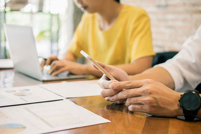 Midsection of colleagues using phone and laptop by graphs on office desk