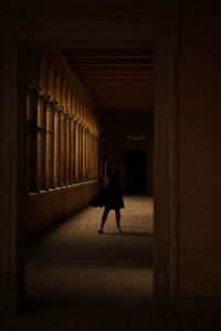 Full length of young woman standing in dark corridor