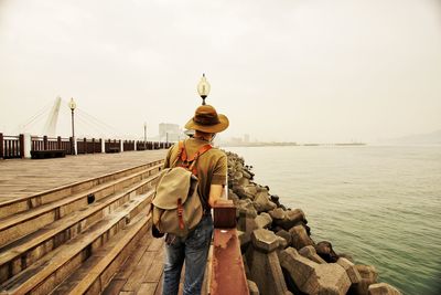 Rear view of man standing by sea against sky