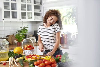 Smiling teenage girl talking over smart phone while standing in kitchen at home