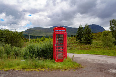 Red telephone booth by road against sky