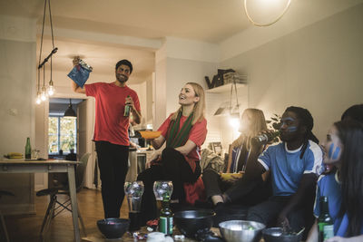 Smiling male and female friends watching soccer match in living room