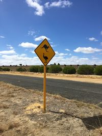 Information sign on road by field against sky