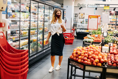 A blonde girl in a protective mask with a grocery basket goes through the store and selects products 