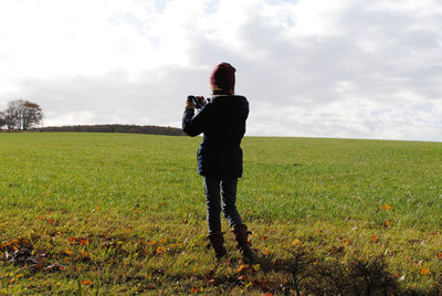 Rear view of woman photographing while standing on field