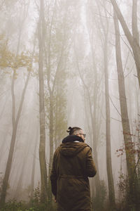 Rear view of man walking in forest during foggy weather