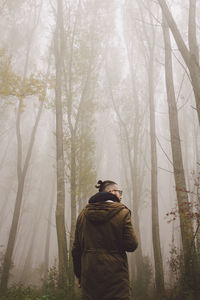 Man standing amidst trees during foggy weather