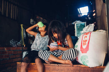 FULL LENGTH OF YOUNG WOMAN USING MOBILE PHONE WHILE SITTING IN KITCHEN