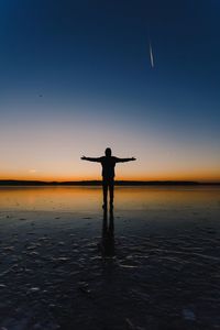 Silhouette of man standing at beach against sky at sunset