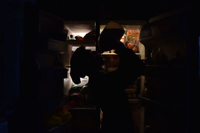 Side view of silhouette man drinking while standing by refrigerator at home