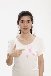 Portrait of woman pointing at breast cancer awareness ribbon against white background