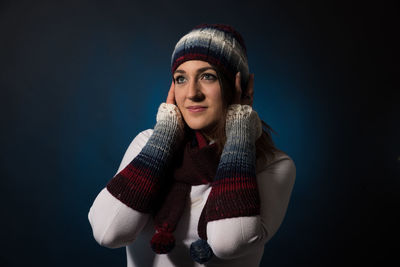 Thoughtful young woman wearing warm clothing against blue background