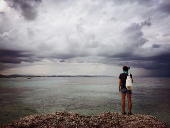 Rear view of woman standing on beach against sky