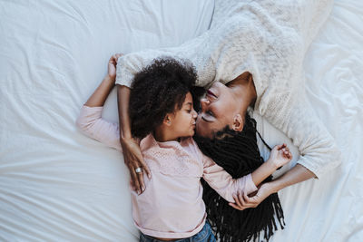 High angle view of daughter kissing mother while lying on bed at home