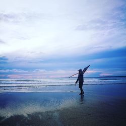 Man walking at beach against cloudy sky during sunset