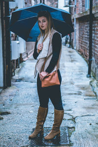 Full length of woman standing with umbrella in alley