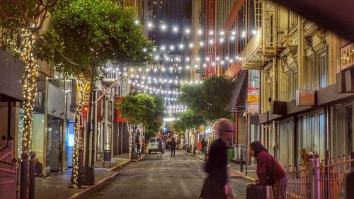 People walking on illuminated street amidst buildings in city at night