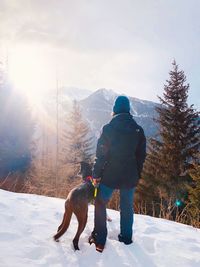 Woman with dog standing on snow against trees