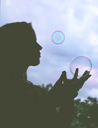 Low angle view of woman holding bubbles against sky