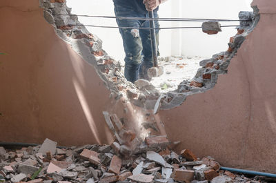 Midsection of construction worker demolishing wall with sledgehammer