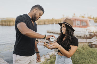 Man pouring wine in wineglass while standing by woman at pier