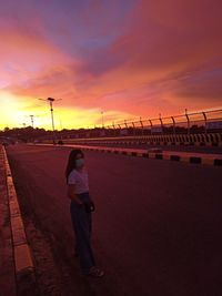 Rear view of man standing on road against orange sky