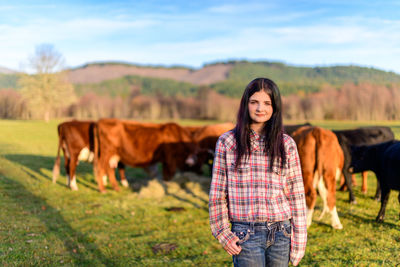 Portrait of smiling young woman standing on field with cattle