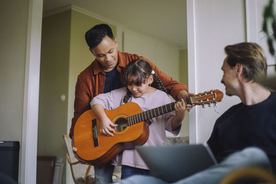 Gay father standing with daughter playing guitar at home