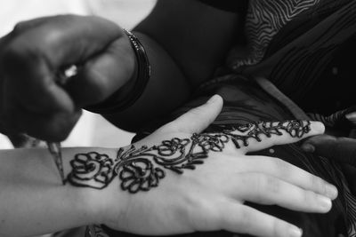 Midsection of woman drawing henna tattoo on hand