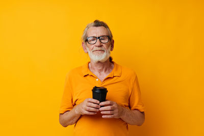 Portrait of young woman holding trophy against yellow background