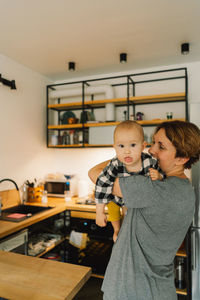 A mother holds her daughter in her arms in the kitchen.