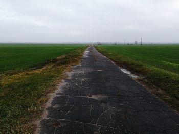 Dirt road amidst field against sky