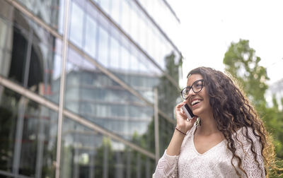 Low angle view of smiling woman talking on phone against building