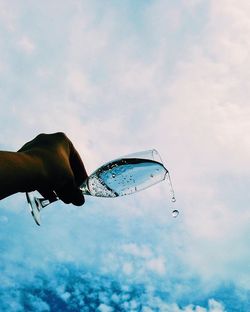 Cropped hand pouring champagne from glass against blue sky