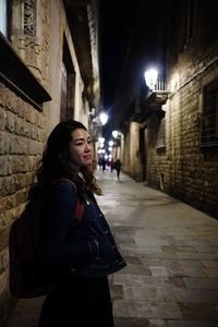 Young woman standing on alley amidst buildings in city