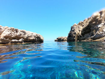 Rocks in sea against clear blue sky