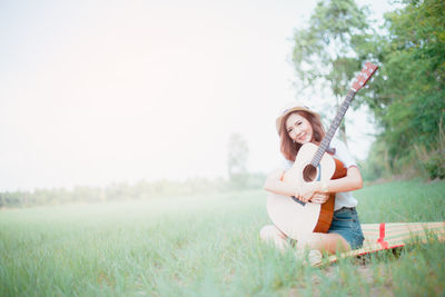 Young woman with guitar on grassy field at park