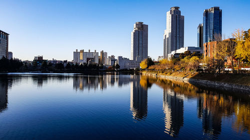Reflection of buildings in lake against clear blue sky