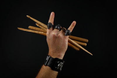 Cropped hand of man holding sticks over black background