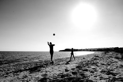 Silhouette people playing with ball on beach against clear sky