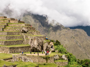 People walking on mountain against cloudy sky
