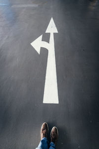 Low section of man standing by arrow sign on road