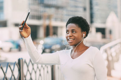 A young african woman in a white sweater and headphones answers a video call while walking down 