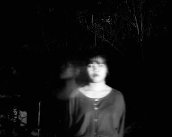 Portrait of woman standing against trees at night