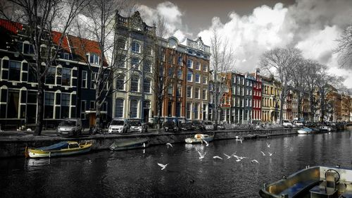 Boats moored in canal by city against sky