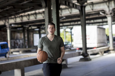 Portrait of young man with basketball standing on bridge