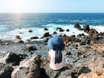 Rear view of woman sitting at beach against clear sky